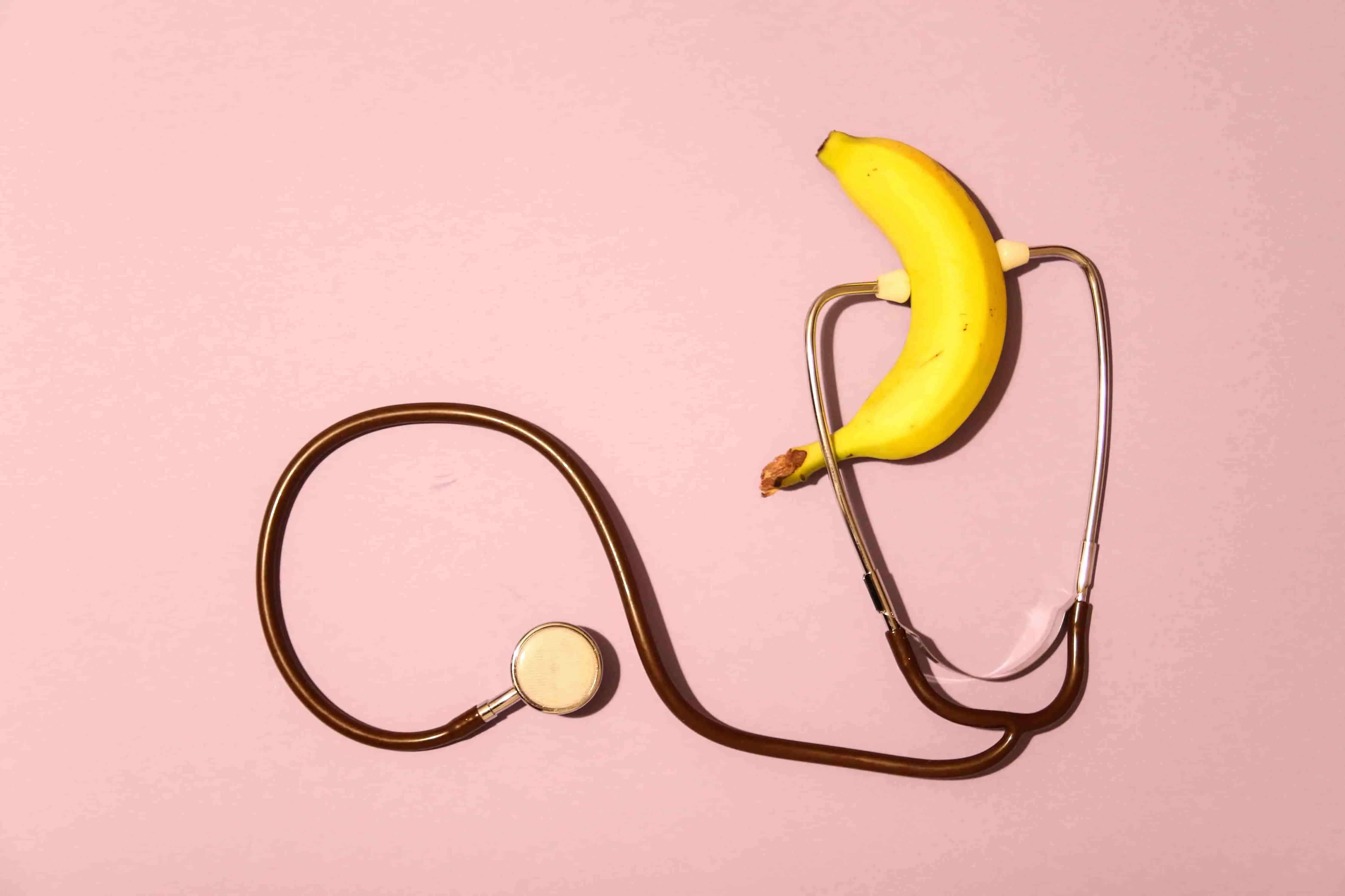 Picture of a stethoscope and a banana on a pink background